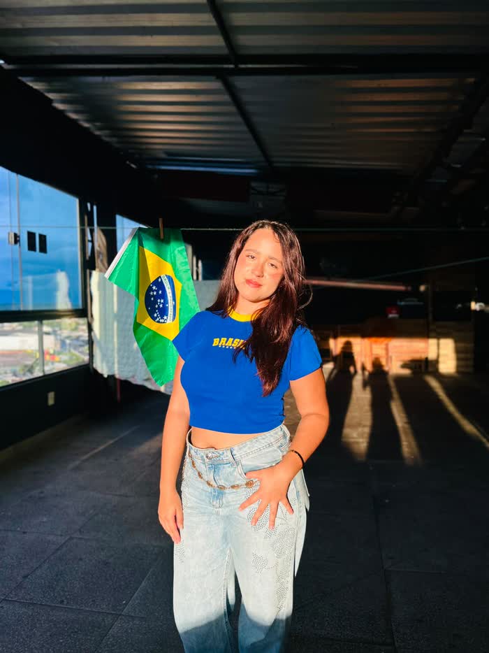 Júlia posando ao lado de uma bandeira do Brasil em um terraço