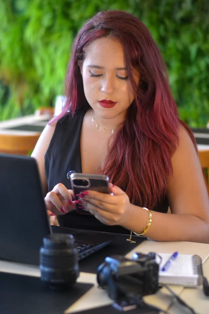 Júlia usando o celular ao lado de laptop, câmera e caderno